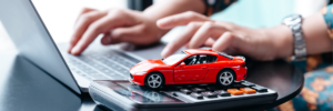 Mani al computer con calcolatrice e modellino di auto rossa per il calcolo della tassazione fringe benefit e welfare aziendale