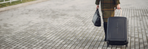 Persona in viaggio d'affari che cammina con trolley rigido nero e borsa da lavoro.